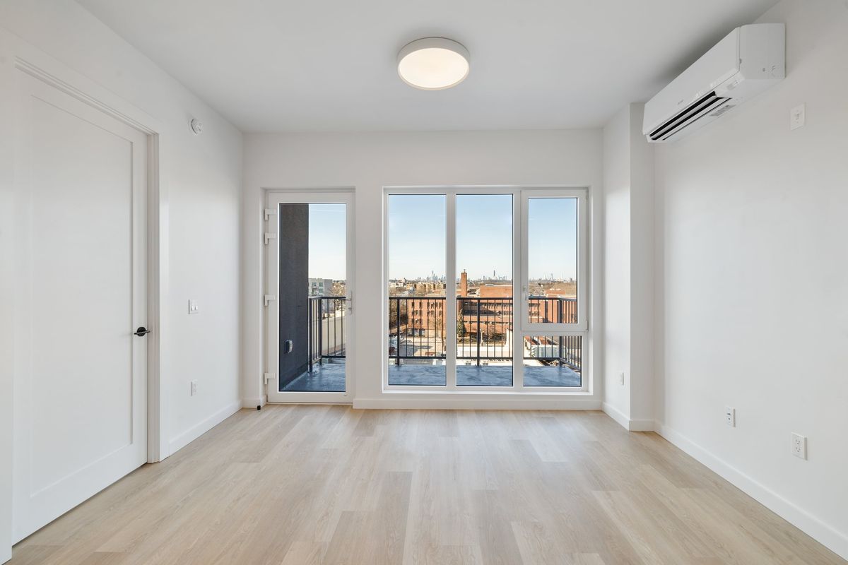 An empty room with a white terrace door between two side lights, looking over rooftops