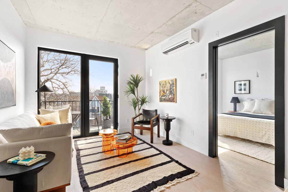 A furnished living room with a black-framed terrace door and side light onto a balcony, bare trees and rooftops beyond