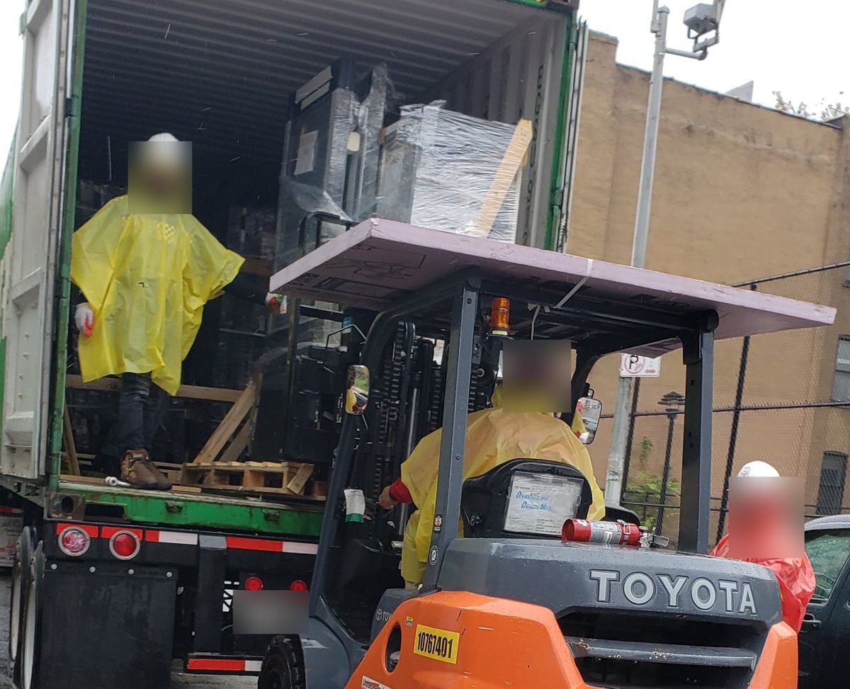 A forklift taking racks out of a shipping container at the kerb