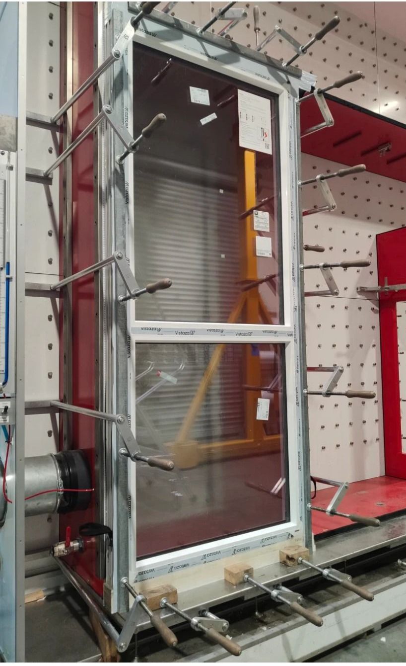 A Vistaza window clamped into the factory test rig, its protective film still on, ready for the air and water test