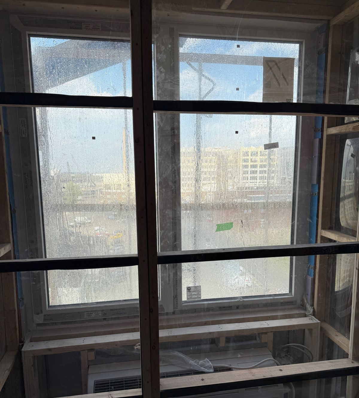 A field water test seen from inside the room: a wood and plastic test chamber sealed over an installed window, with water running down the outside of the glass