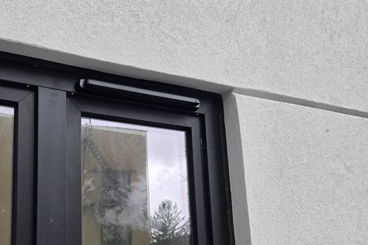 A black vent canopy across the head of a black window frame, seen from below