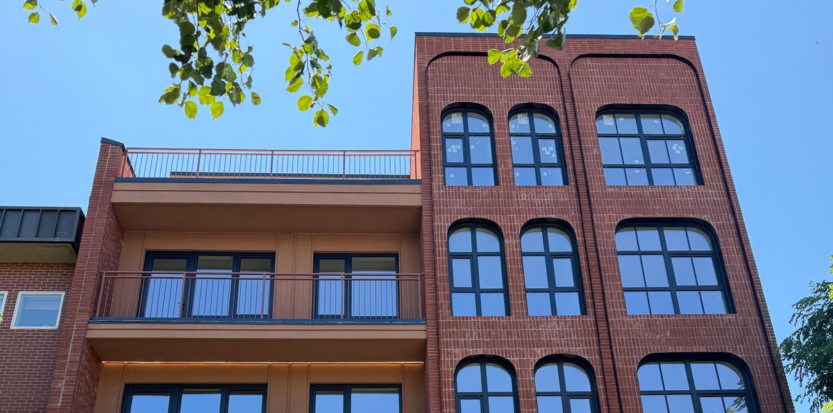 A flush red-brick bay of radius-headed black windows beside a roof terrace, on a Brooklyn condominium
