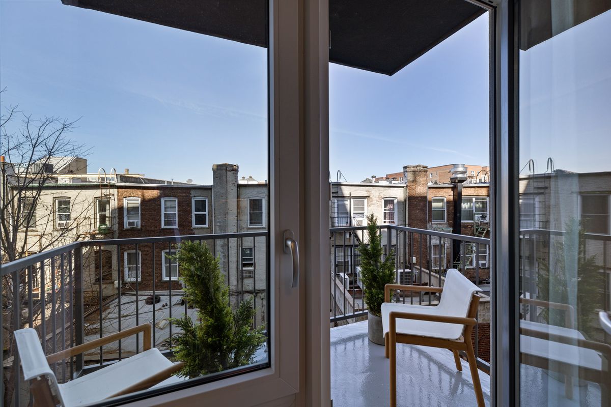 Looking out through an open white terrace door and corner glazing onto a balcony with chairs