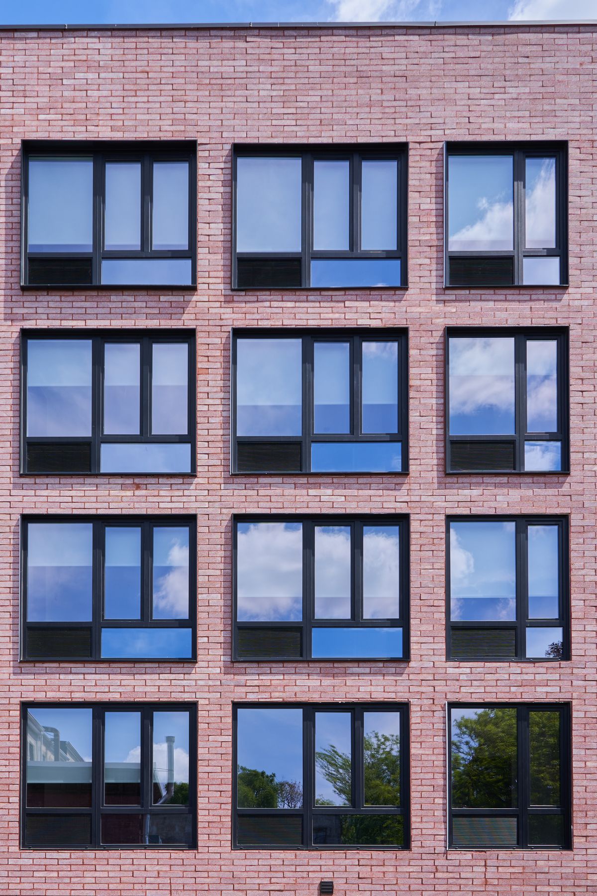 A brick elevation seen flat on: four floors of black windows, each with a louver at the foot of its left-hand lite