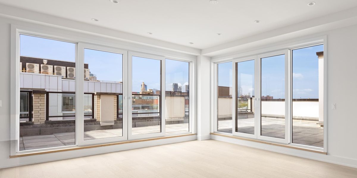Two four-panel sliding doors meeting at the corner of a bright empty room, with the terrace and skyline beyond