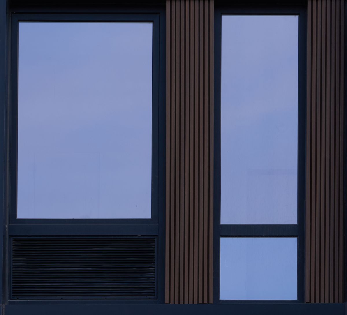 A black window seen square on from outside: a large fixed lite over a louver in the same frame, and a narrow lite beside it between wood-look slats