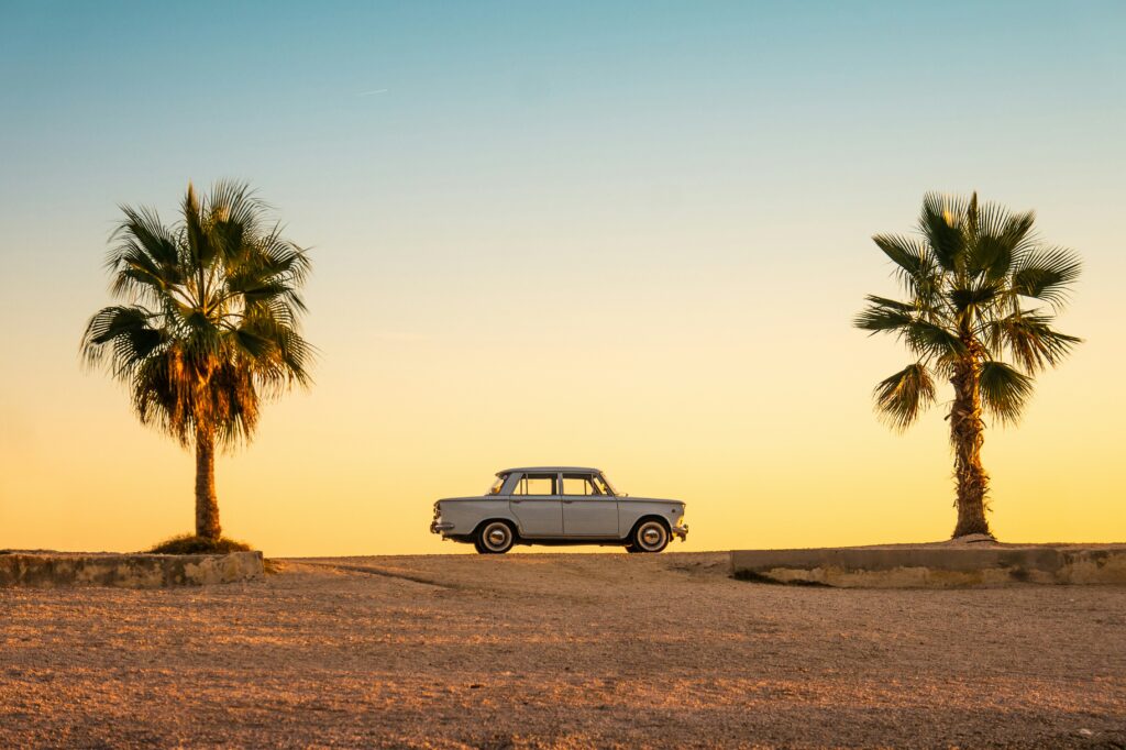 A retro car surrounded by sand and two palm trees—courtesy of Unsplash.